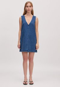 Blauwe mouwloze jurk met een diepe V-hals en een losse, ontspannen pasvorm. Heeft een subtiel patroon en een rechte zoom op knielengte.