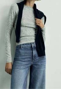 Harmaa pitkähihainen paita yhdistetty korkeavyötäröisiin vaaleansiniraitoisiin leveälahkeisiin farkkuihin. Tummansininen neuletakki roikkuu harteilla. Sileät tekstuurit.