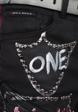 Un pantalon en denim noir présente un design blanc "ONE" bordé d'œillets en métal. Comprend une poche avec une étiquette de logo et un détail zippé.