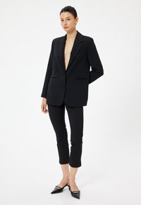 Svart blazer med djup V-ringning och två knappar. Matchat med åtsittande svarta byxor och spetsiga svarta klackar. Slät tygstruktur.