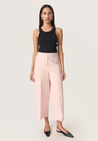 Sort ribbet tanktop uden ærmer parret med højtaljede lyserøde vidde bukser. Modellen bærer skinnende sorte slingback sko.