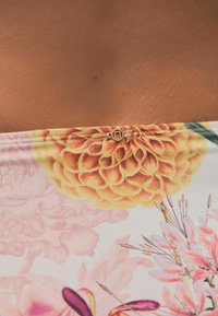 Blommig bikiniöverdel med stora gula dahlia och rosa blommönster, med en gyllen accentdetalj i mitten. Mjuk, flerfärgad tyg.