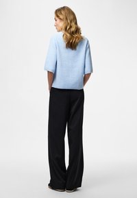 Jasnoniebieski dzianinowy sweter z krótkimi rękawami, zestawiony z czarnymi szerokimi spodniami w prążki. Strój cechuje się luźnym krojem i miękką fakturą.