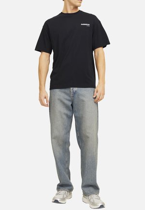 T-shirt en coton noir, à manches courtes, avec le texte « PARADISE ». Porté avec un jean en denim bleu clair, coupe décontractée, uni, sans motifs visibles.