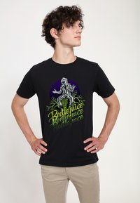 Sort bomulds t-shirt med et grafisk design af en karakter iført stribede klæder, med gul tekst "Beetlejuice" og en lilla cirkel baggrund.
