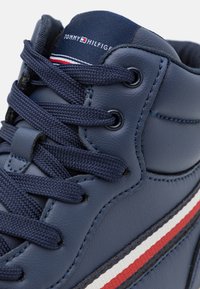 Sneaker alta blu navy in pelle testurizzata, con lacci intrecciati e un accento di striscia bianca e rossa. Branding sulla linguetta.
