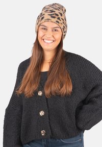 Black knitted cardigan with three decorative gold buttons, worn over a black top. Beige beanie with a brown leopard print pattern.