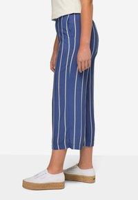 Modré a bílé pruhované kalhoty s širokým střihem, hladkým povrchem, elastickým pasem a bočními kapsami, doplněné o bílé platformové tenisky.