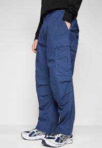 Siniset kuormahousut, jotka on valmistettu kevyestä kankaasta. Housuissa on rento istuvuus, joustava vyötärönauha, sivutaskut ja kerrokselliset kuormataskut.