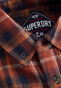 Rudekulet flannel-skjorte i brændt orange og marineblå med en tekstureret vævning, knaplukning og en etiket med teksten "Superdry Shirting Co."