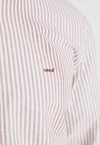 Red and white striped shirt featuring a small, embroidered Levi's logo on the chest. Fabric appears smooth with a lightweight texture.