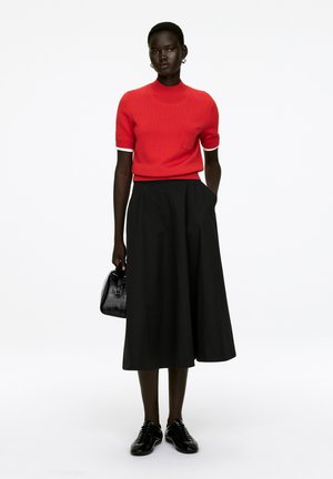 Red knit short-sleeve sweater with a small pocket, paired with a black high-waisted, full-length skirt, and black lace-up shoes. Black handbag included.