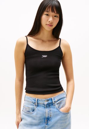 Tirantes finos, top de algodón negro ajustado. Presenta un pequeño logo blanco de "Tommy Jeans" en el pecho. Combinado con unos jeans de color azul claro.