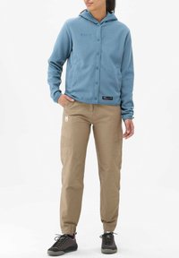 Fleece hooded jacket in light blue with button closure and two front pockets, paired with tan cargo pants featuring side pockets and elastic cuffs.