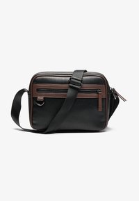 Sac messager noir en tissu texturé, avec un accent en cuir marron, une bandoulière réglable et une poche avant zippée.