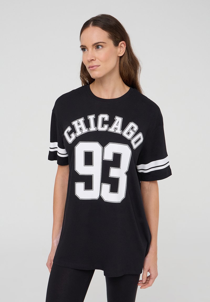 T-shirt oversize nera in cotone, con la scritta "CHICAGO" e "93" in stampa bianca bold, e dettagli a righe bianche sulle maniche corte.