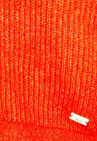 Fel oranje gebreide stof met een klein wit rechthoekig label bevestigd vlak bij de rechteronderhoek.