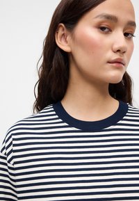 Ναυτικό μπλε και λευκή ριγέ βαμβακερή μπλούζα με στρογγυλή λαιμόκοψη. Το ύφασμα έχει απαλή υφή και οι ρίγες είναι ομοιόμορφα spaced.