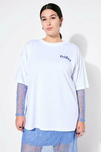 Bílé oversized tričko s potiskem "Pátek" v námořnické modři. Pod ním dlouhé rukávy a sukně z modré krajky dodávají texturu a kontrast.