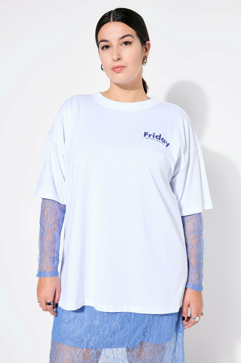 Bílé oversized tričko s potiskem "Pátek" v námořnické modři. Pod ním dlouhé rukávy a sukně z modré krajky dodávají texturu a kontrast.
