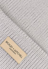 Szary dzianinowy materiał o prążkowanej teksturze z widoczną beżową metką z napisem "BICKLEY + MITCHELL AMSTERDAM" przyszytą na nim.