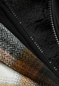 Black zip detail with plush black lining, alongside textured fabric featuring a herringbone pattern in brown, gray, and cream tones.