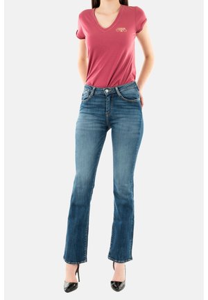 T-shirt rose en V avec des manches retroussées, associé à un jean droit bleu. Détails notables incluent une boucle en argent et une texture délavée.