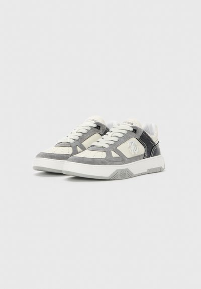 Un paio di sneaker basse in bianco, camoscio grigio e accenti neri con lacci bianchi e logo del marchio sul lato e sulla linguetta.