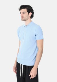 Polo shirt azzurro chiaro a maniche corte con chiusura a zip, tessuto testurizzato, colletto e polsini a costine, abbinato a pantaloni neri con cordini.