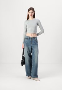 Lys grå langermet cropped topp satt sammen med høyt liv, vide blå jeans. Modellen holder en svart veske og har på seg lyse sko.
