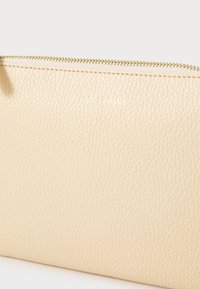 Beige leather clutch with a textured surface, featuring a gold zipper and the brand name embossed in gold on the front.