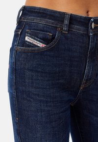 Mörkblå denimjeans med en figurnära design, med orange sömmar, en liten framficka och en synlig logotagg på bakfickan.