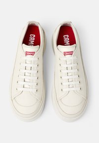 Sneaker in pelle bianca con punta arrotondata, lacci bianchi e fodera interna rossa. Presenta una piccola etichetta rossa "CAMPER" sulla linguetta.