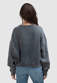 Ciemnoszara, oversize bluza z zaokrąglonym dekoltem, opuszczonymi ramionami i prążkowanymi mankietami. Materiał wydaje się miękki z wyblakłą teksturą.