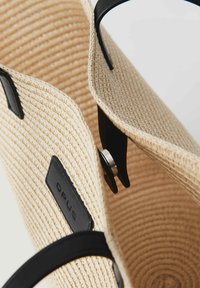 Borsa tote in paglia intrecciata con manici e dettagli in pelle nera; presenta un fondo rotondo e un dettaglio di chiusura metallica all'apertura.