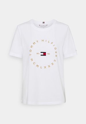 Biała koszulka z krótkim rękawem z okrągłym złotym napisem „TOMMY HILFIGER MCMLXXXV” i małym czerwono-biało-niebieskim logo Tommy Hilfiger na środku.