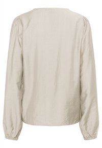 Blouse beige clair à manches longues avec un col rond, des épaules froncées et des poignets élastiques. Tissu doux et texturé avec un léger éclat.