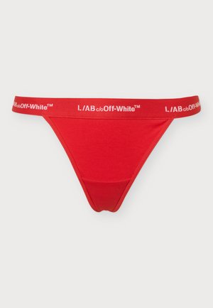 Mujer de pie con las manos relajadas a los lados, vistiendo ropa interior roja de dos piezas con bandas elásticas blancas con marca, sobre un fondo claro y liso.