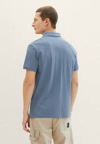 Hellblaues Poloshirt mit einem Kragen, kurzen Ärmeln und einem geraden Saum. Hergestellt aus weichem Stoff mit glatter Textur.