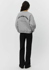 Gray oversized sweatshirt with black text on the back, paired with black pants featuring white polka dots. Casual, relaxed design.