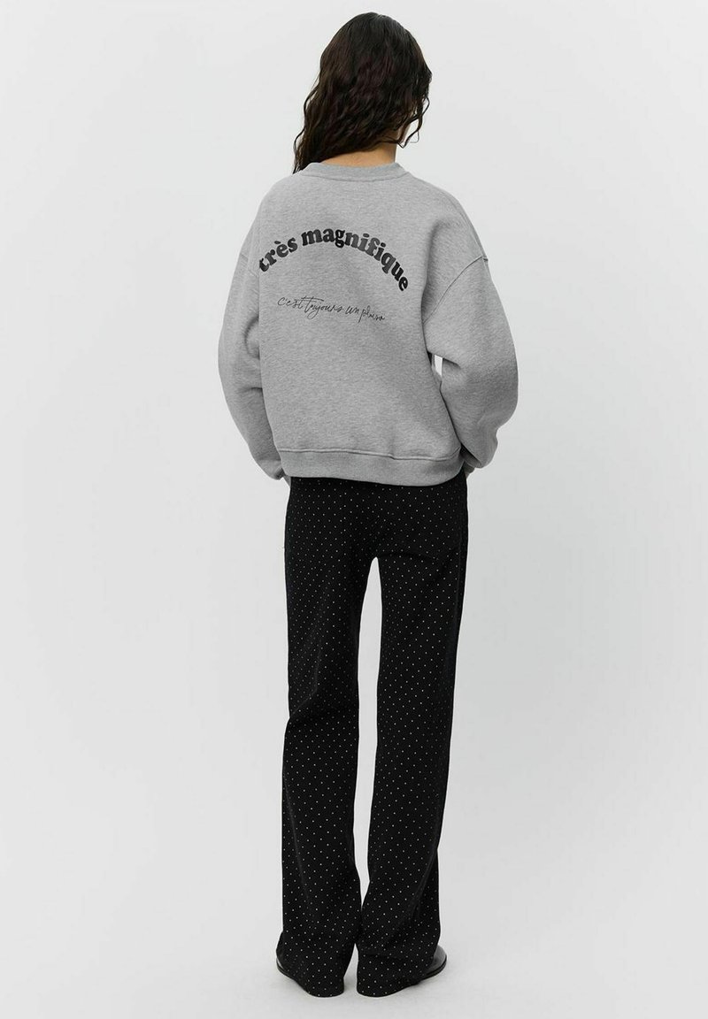 Gray oversized sweatshirt with black text on the back, paired with black pants featuring white polka dots. Casual, relaxed design.