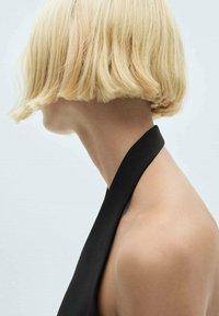 Blond bob-frisure med teksturerede ender. Sort halterneck-top, der viser glat hud på skulderen og nakken mod en lys baggrund.