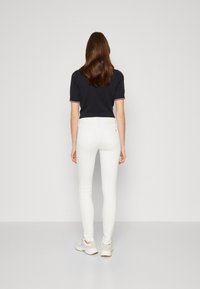 Jeans blancos ajustados con una textura suave y detalles de costura sutiles, combinados con un polo oscuro con un ribete rojo y blanco en el cuello.