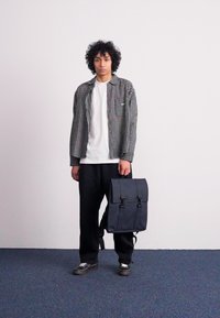 Chemise à carreaux noir et blanc, t-shirt blanc, pantalon noir large, et un sac à dos bleu foncé avec des bretelles doubles et des boucles.