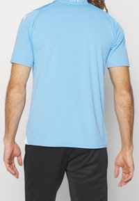 Maglia da atletica azzurro chiaro con maniche corte, collo arrotondato e accenti bianchi sulle spalle; realizzata in tessuto sintetico traspirante.
