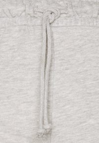 Gros plan sur un tissu gris clair avec un cordon noué passé dans la ceinture d’un pantalon de jogging doux.