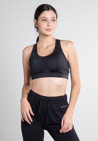 Svart sport-BH med en slät yta, med racerback-design och meshpaneler för andningsförmåga. Paret med svarta byxor med dragsko.