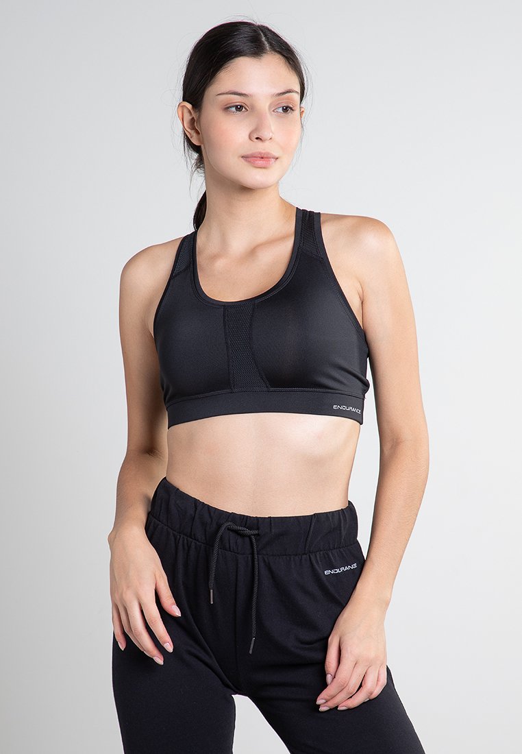 Svart sport-BH med en slät yta, med racerback-design och meshpaneler för andningsförmåga. Paret med svarta byxor med dragsko.