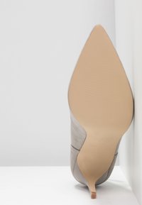 Chaussure à talon haut en daim gris avec bout pointu et design élégant. Dispose d'une semelle couleur nude avec un détail de texture antidérapante.