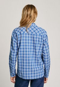 Blue plaid shirt with long sleeves, button cuffs, and a back yoke detail. The material appears lightweight and textured with alternating patterns.